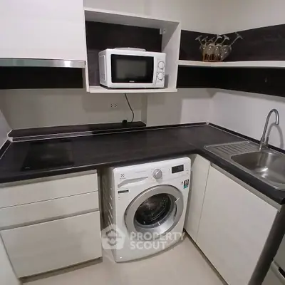Modern compact kitchen with washing machine and microwave, sleek countertops, and ample storage.