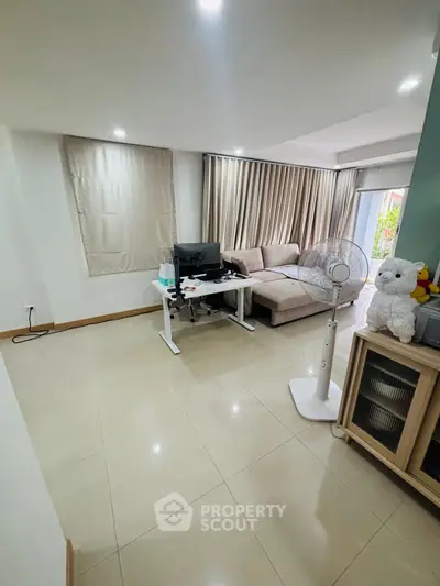 Spacious living room with modern decor and natural light, featuring a cozy sofa and work desk.