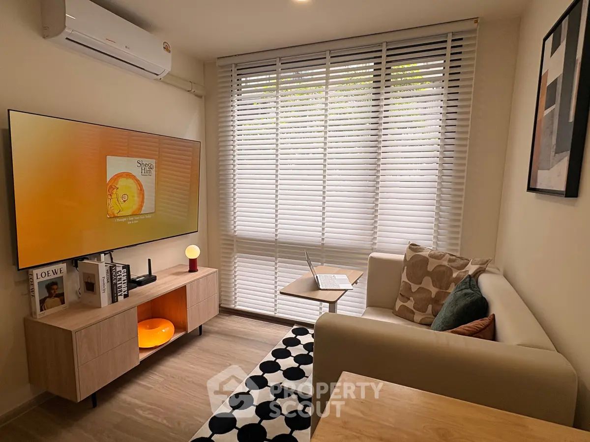 Cozy living room with modern decor, featuring a wall-mounted TV, stylish sofa, and large window with blinds.