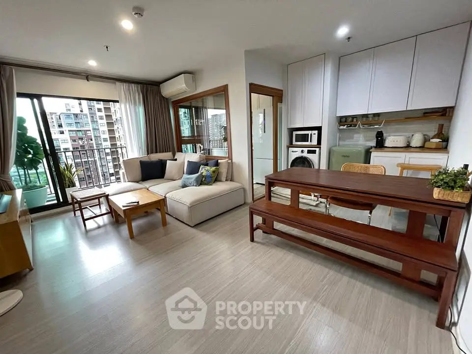 Modern living room with open kitchen, featuring stylish furniture and city view balcony.