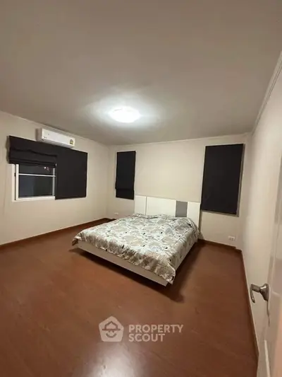 Spacious bedroom with modern decor and wooden flooring, featuring a cozy bed and air conditioning.