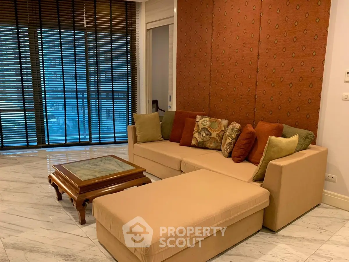 Elegant living room with stylish sofa and marble flooring, featuring large windows with wooden blinds.