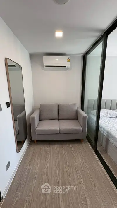 Modern compact living space with sofa and air conditioning, featuring sleek wooden flooring.
