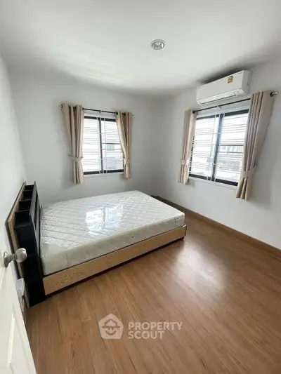 Bright bedroom with wooden flooring and large windows in modern apartment.