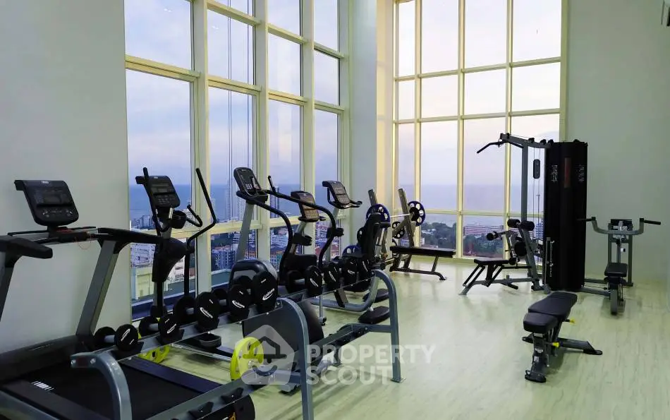 Spacious gym with modern equipment and stunning city view through large windows.