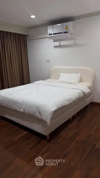 Cozy bedroom with wooden flooring and modern air conditioning unit, perfect for restful nights.