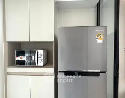 Modern kitchen with sleek fridge and microwave in a minimalist design.