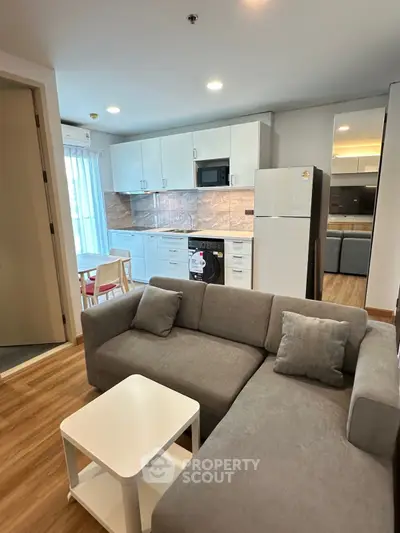 Modern open-layout living room with kitchen, featuring sleek appliances and cozy seating area.