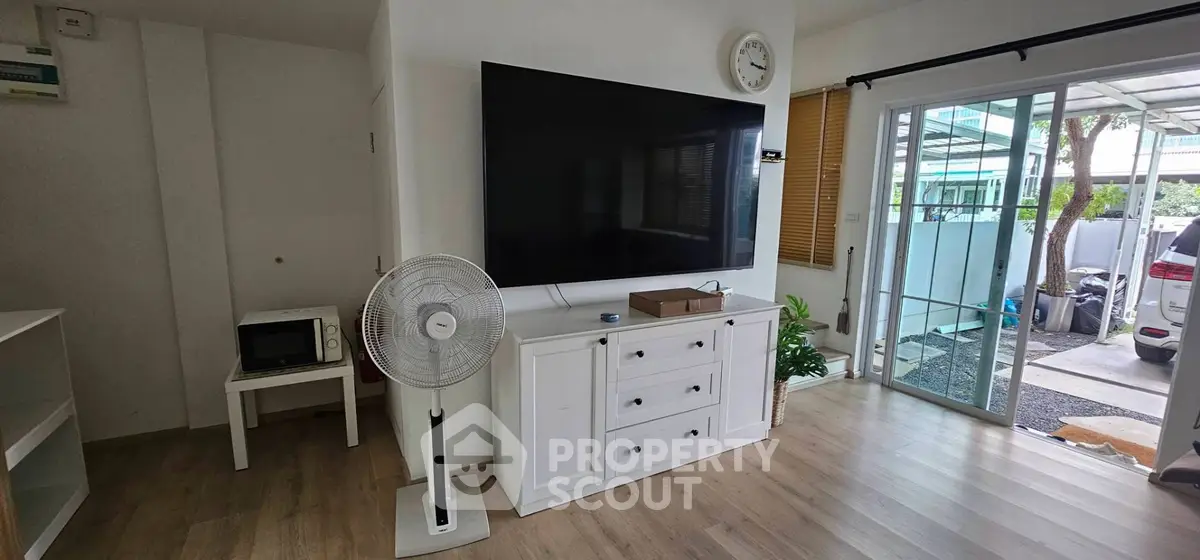 Modern living room with large TV, fan, and sliding glass doors leading to a carport.