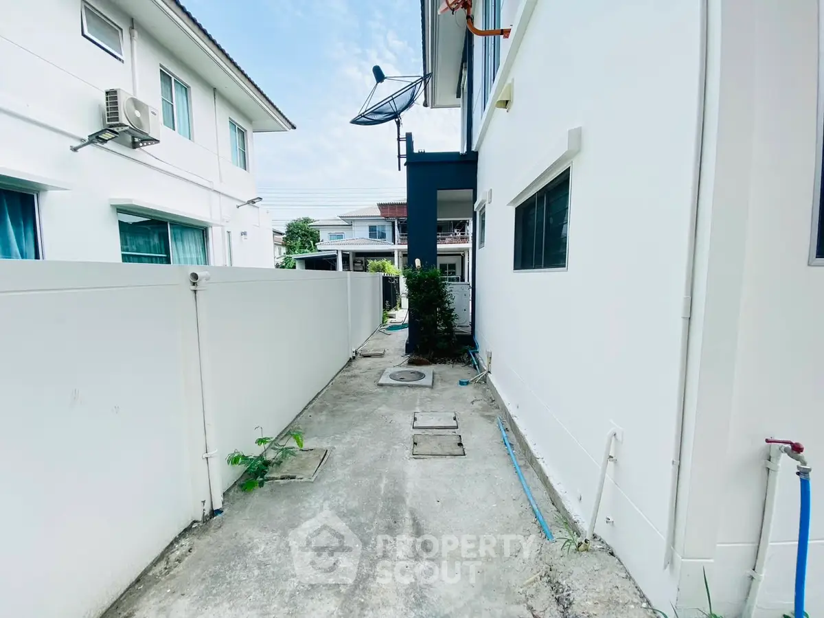 Modern residential exterior with clean white walls and satellite dish, showcasing a neat side pathway.