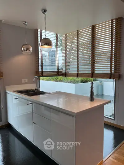 Modern kitchen with sleek white cabinetry and large windows offering a lush garden view.