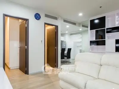 Modern living room with white leather sofa and open doorways, featuring sleek shelving and wooden flooring.