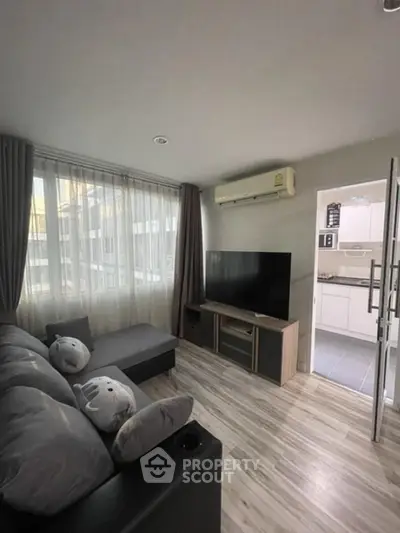 Cozy living room with modern decor and large TV, adjacent to a sleek kitchen.