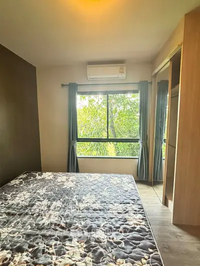 Cozy bedroom with large window and air conditioning, offering a serene view of lush greenery.
