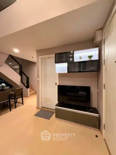 Modern living room with sleek TV unit and stylish shelving, featuring a cozy dining area and staircase.