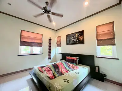 Cozy bedroom with modern decor and ceiling fan, featuring natural light from two windows.