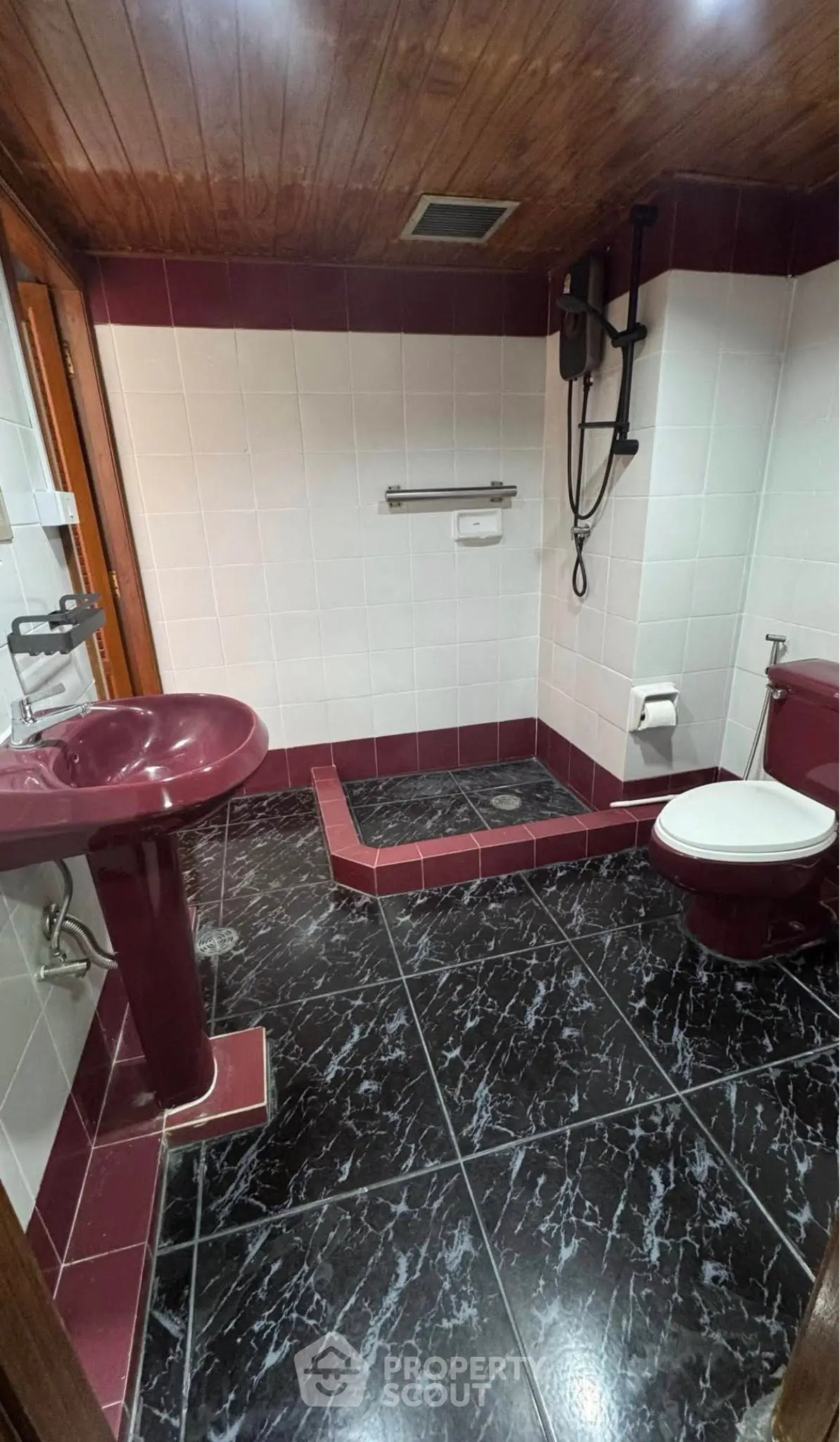 Elegant bathroom with maroon fixtures and black marble tiles, featuring a unique shower area.