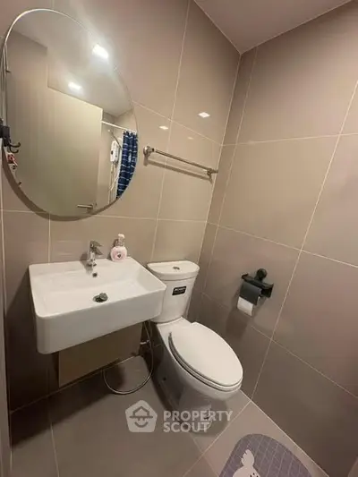 Modern bathroom with sleek fixtures and neutral tiles, featuring a round mirror and compact sink.