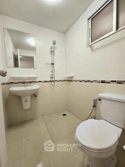 Modern bathroom with sleek fixtures and neutral tiles, featuring a shower and toilet.