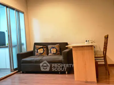 Cozy living room with sofa and dining table, featuring wooden flooring and sliding glass doors.