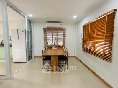 Modern dining area with wooden table and blinds, adjacent to a sleek kitchen.