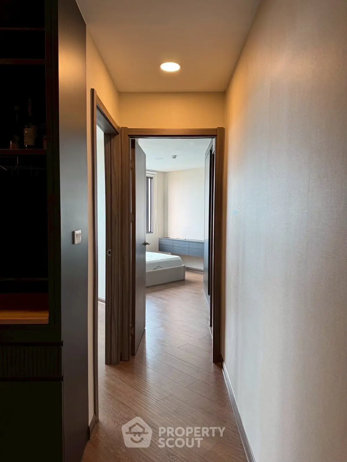 Modern apartment hallway leading to a bright bedroom with wooden flooring and neutral walls.