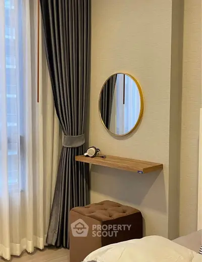 Elegant bedroom corner with round mirror and plush stool, featuring luxurious curtains.
