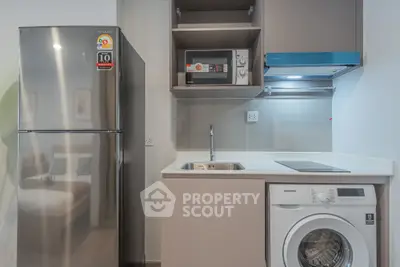 Modern kitchen with stainless steel fridge, microwave, and washing machine in compact layout.