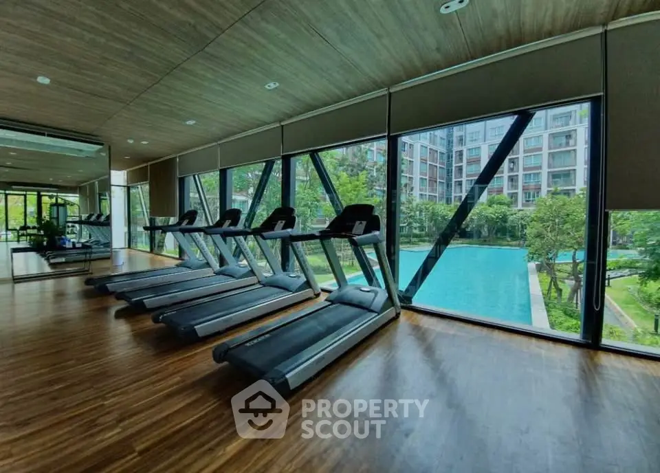 Modern gym with treadmills overlooking a stunning pool view in luxury apartment complex.