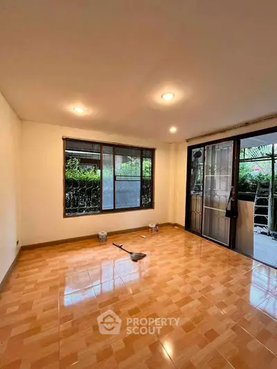 Spacious living room with large windows and tiled flooring, perfect for natural light and comfort.