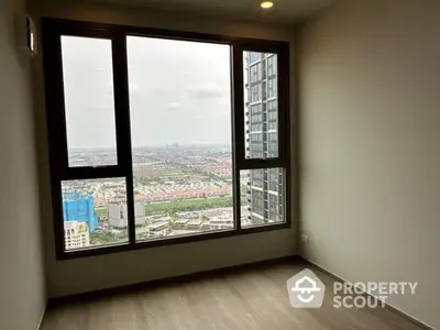 Spacious room with large window offering stunning cityscape view in modern high-rise building.