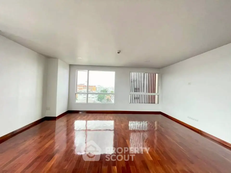 Spacious living room with polished wooden floors and large windows offering city views.