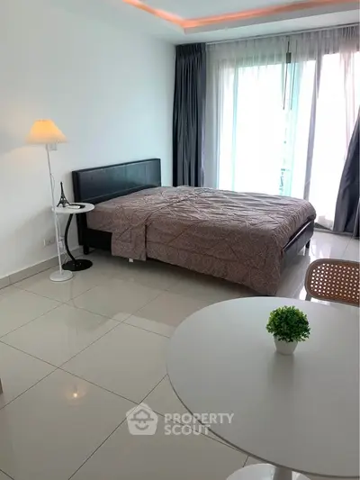 Modern bedroom with sleek design, featuring a cozy bed, stylish lamp, and natural light from large windows.