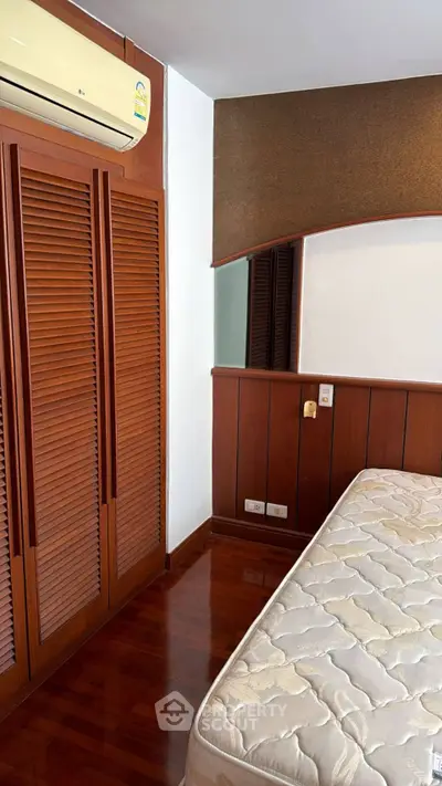 Cozy bedroom with wooden flooring and built-in wardrobe, featuring air conditioning for comfort.
