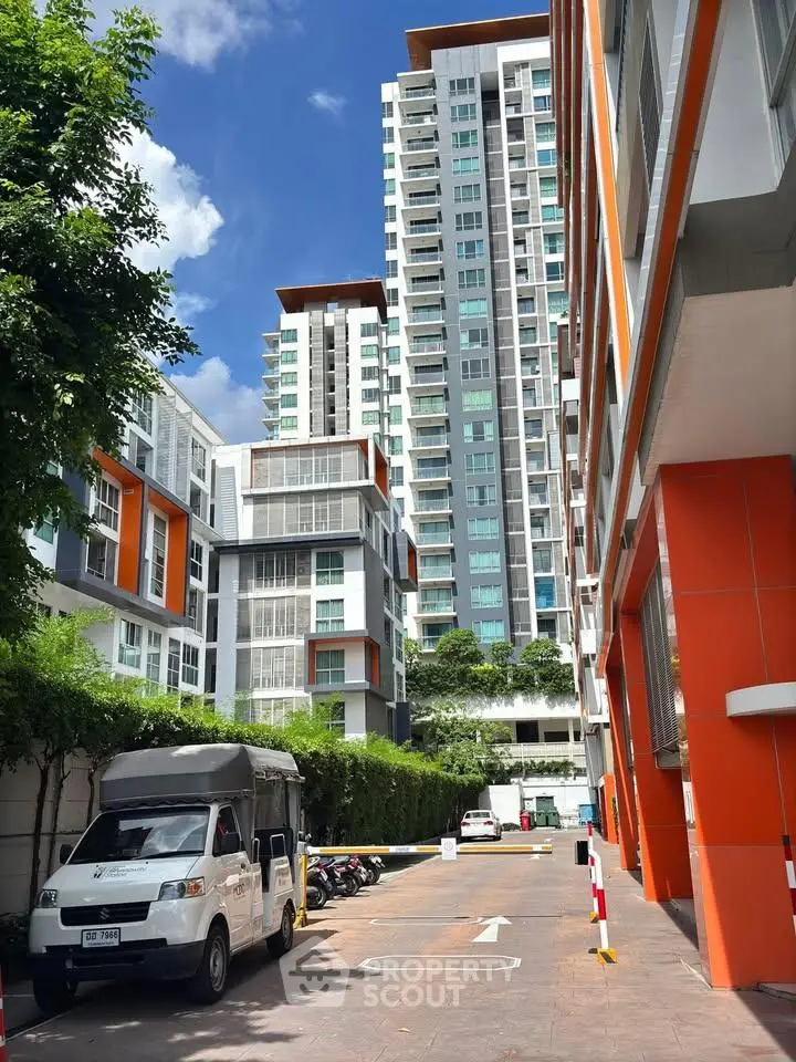 Modern high-rise residential building with vibrant orange accents and lush greenery.