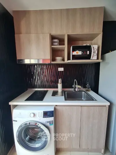 Compact modern kitchen with washing machine and microwave, ideal for urban living.