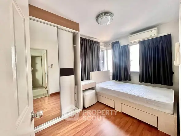 Cozy bedroom with wooden flooring, mirrored wardrobe, and ample natural light from large windows.