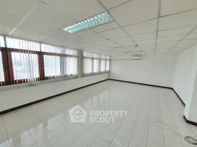 Spacious empty room with tiled flooring and large windows, ideal for office or studio space.