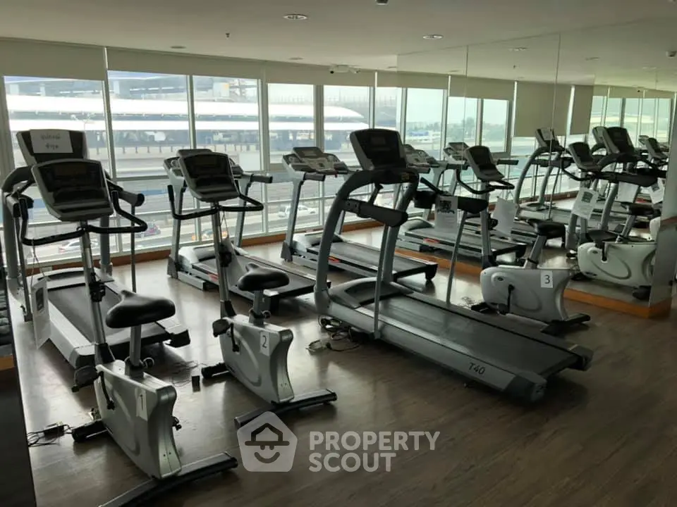 Modern gym with treadmills and exercise bikes in a high-rise building with city views.