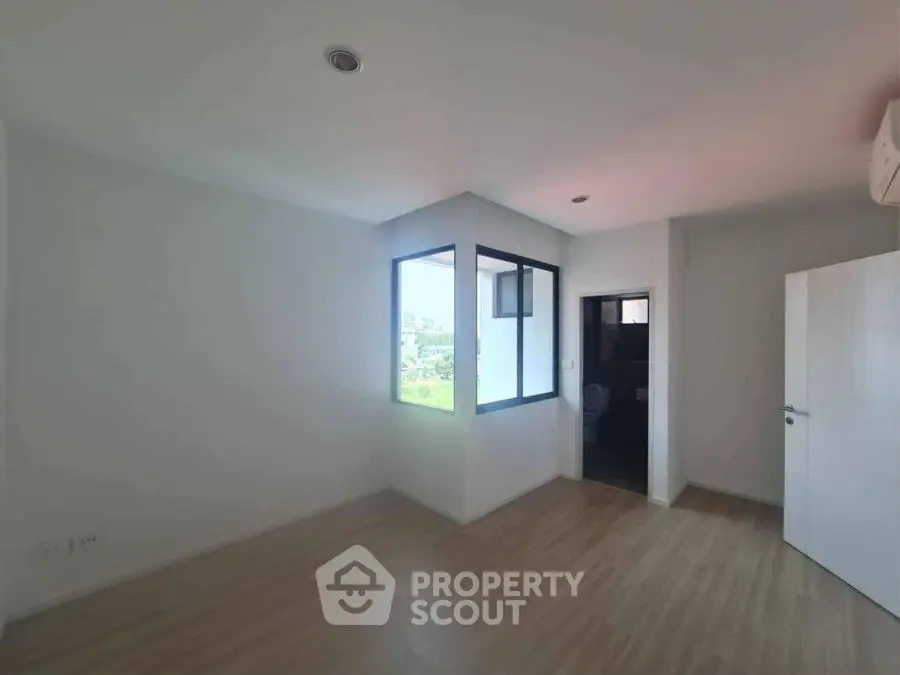 Spacious empty room with large window and wooden flooring, ideal for customization.