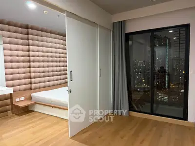 Modern bedroom with sliding doors and city view, featuring wooden flooring and stylish decor.