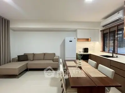 Modern living room with stylish sofa and dining area, featuring sleek kitchen appliances and elegant decor.
