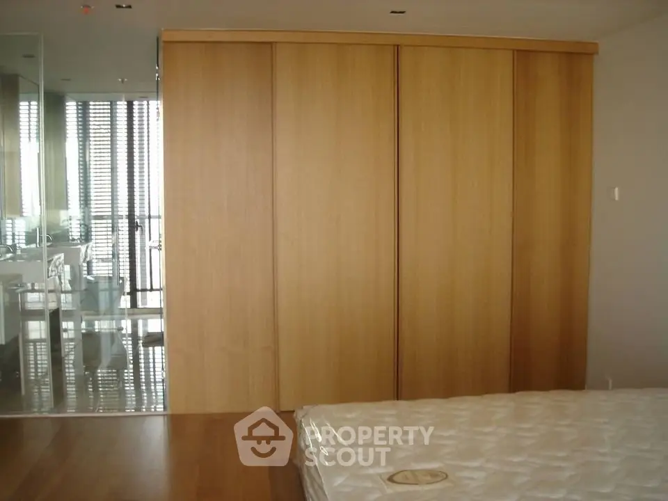 Spacious bedroom with wooden flooring and large built-in wardrobe, offering modern and sleek design.