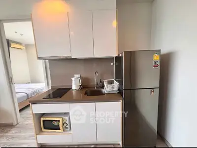 Modern compact kitchen with fridge, microwave, and sleek cabinetry in cozy apartment.