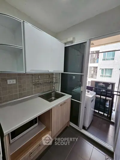 Modern kitchen with open layout and balcony view, featuring sleek cabinetry and washing machine.