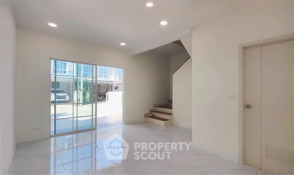 Spacious modern living room with large windows and staircase in a bright home.
