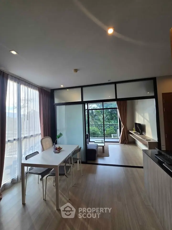 Spacious modern living room with large windows and balcony view, featuring sleek furniture and natural light.