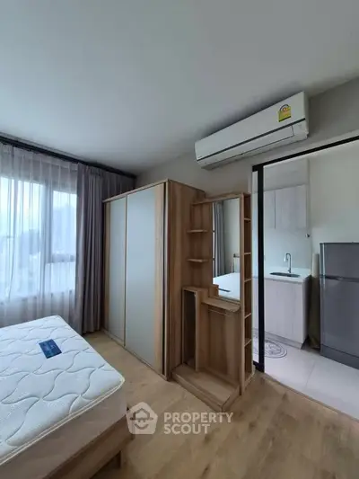 Modern bedroom with wooden furniture and air conditioning, adjacent to a compact kitchen area.