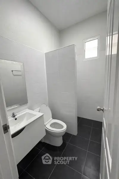 Modern bathroom with sleek black tiles and white fixtures, featuring a compact design and natural light.