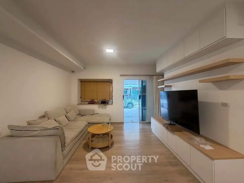 Modern living room with cozy sofa and large TV, featuring sleek storage and natural light.